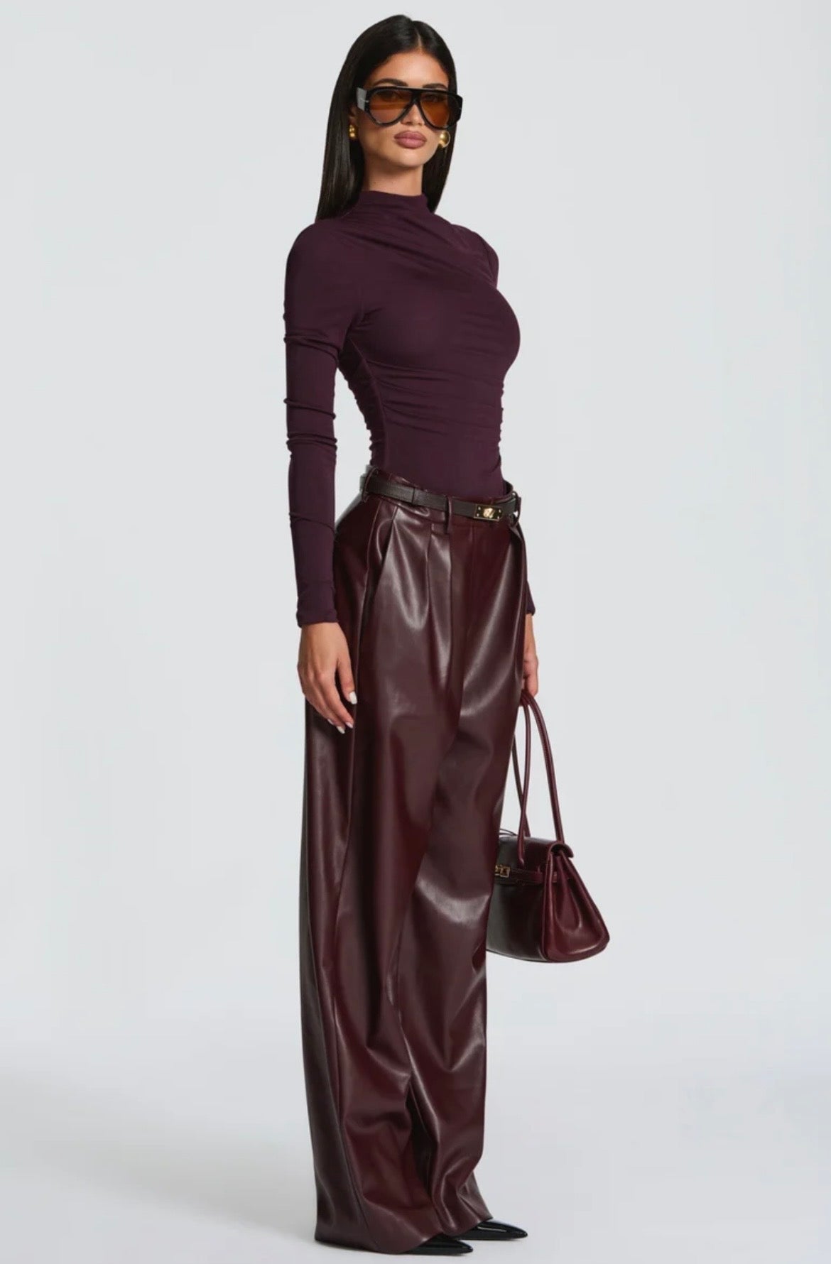 Pantalone Palazzo in Faux Leather Caratterizzato da una gamba ampia palazzo e doppie pinces frontali, dona un movimento sofisticato a ogni passo. La cintura sottile coordinata con fibbia metallica dorata definisce il punto vita.