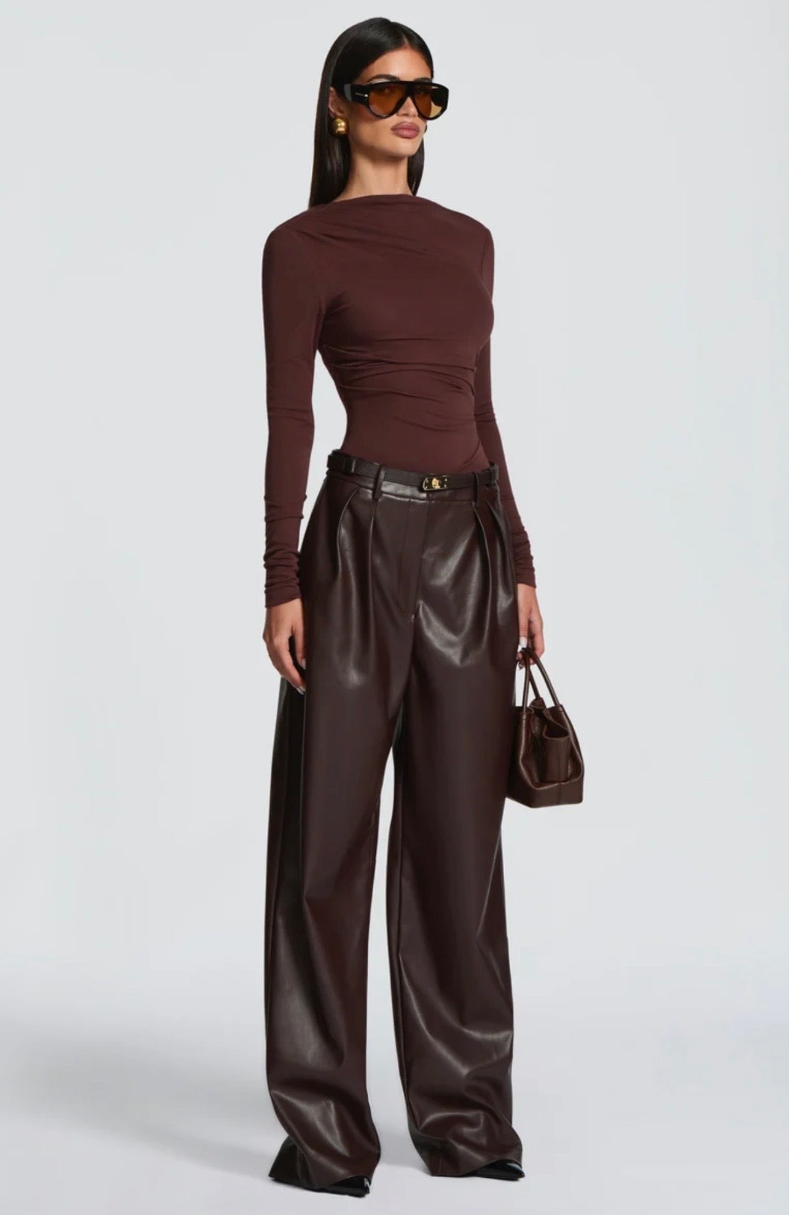 Pantalone Palazzo in Faux Leather Caratterizzato da una gamba ampia palazzo e doppie pinces frontali, dona un movimento sofisticato a ogni passo. La cintura sottile coordinata con fibbia metallica dorata definisce il punto vita.