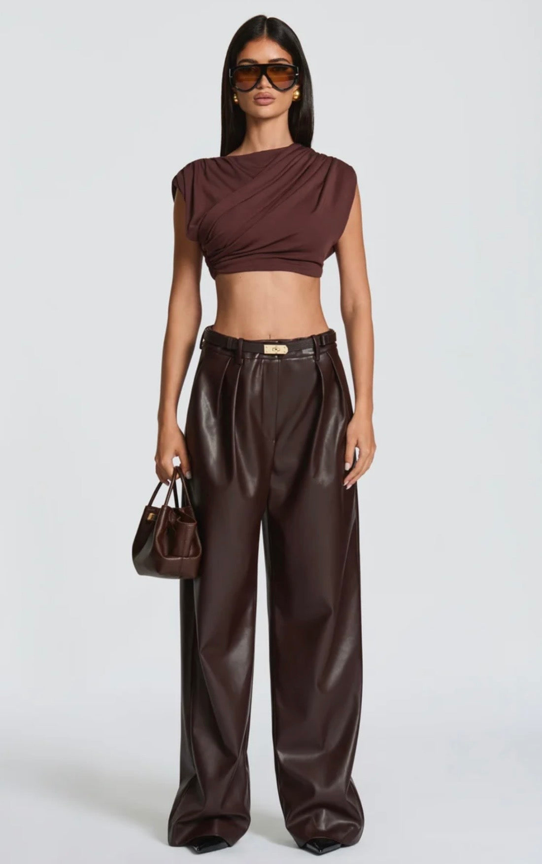 Pantalone Palazzo in Faux Leather Caratterizzato da una gamba ampia palazzo e doppie pinces frontali, dona un movimento sofisticato a ogni passo. La cintura sottile coordinata con fibbia metallica dorata definisce il punto vita.
