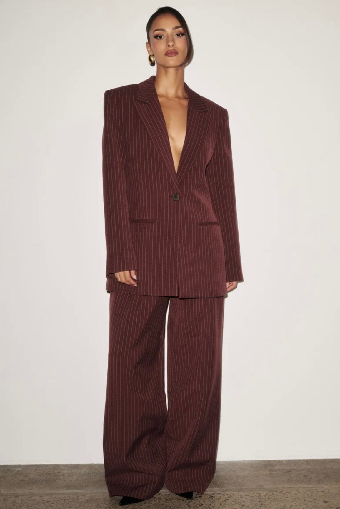 L'essenza del Tailleur Ilary contemporaneo gessato. Questo set coordinato combina un blazer monopetto strutturato a spalla definita con pantaloni palazzo a gamba larga caduta fluida. Il motivo gessato sottile regala una silhouette slanciata ed elegante