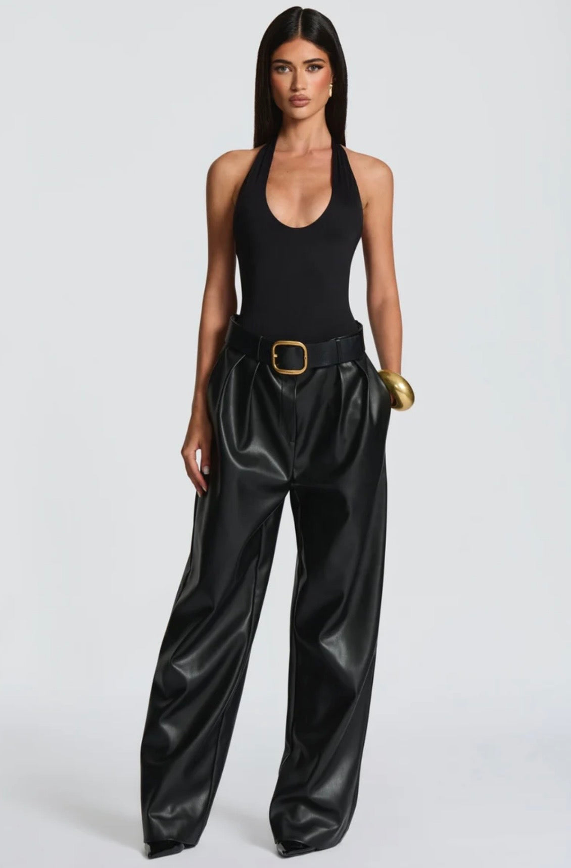 Pantalone Palazzo in Faux Leather Caratterizzato da una gamba ampia palazzo e doppie pinces frontali, dona un movimento sofisticato a ogni passo. La cintura sottile coordinata con fibbia metallica dorata definisce il punto vita.