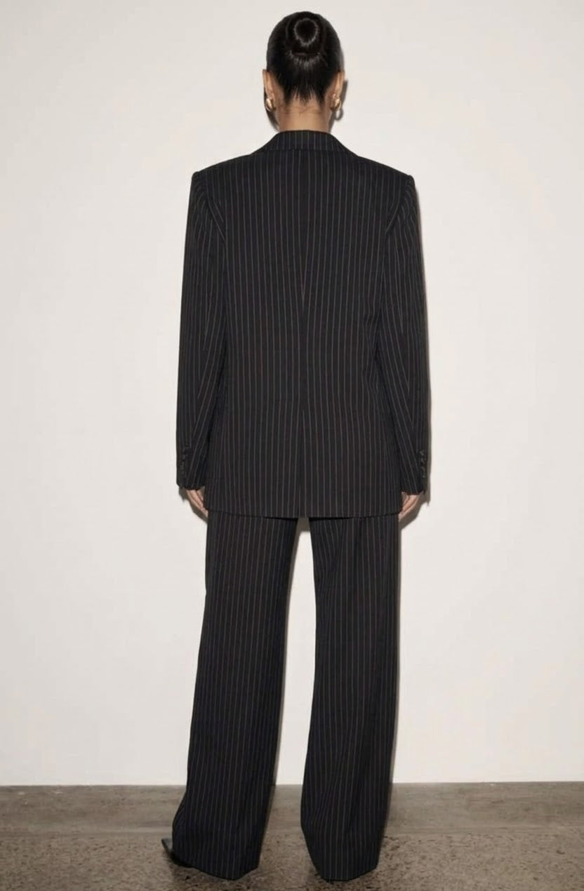 L'essenza del Tailleur Ilary contemporaneo gessato. Questo set coordinato combina un blazer monopetto strutturato a spalla definita con pantaloni palazzo a gamba larga caduta fluida. Il motivo gessato sottile regala una silhouette slanciata ed elegante